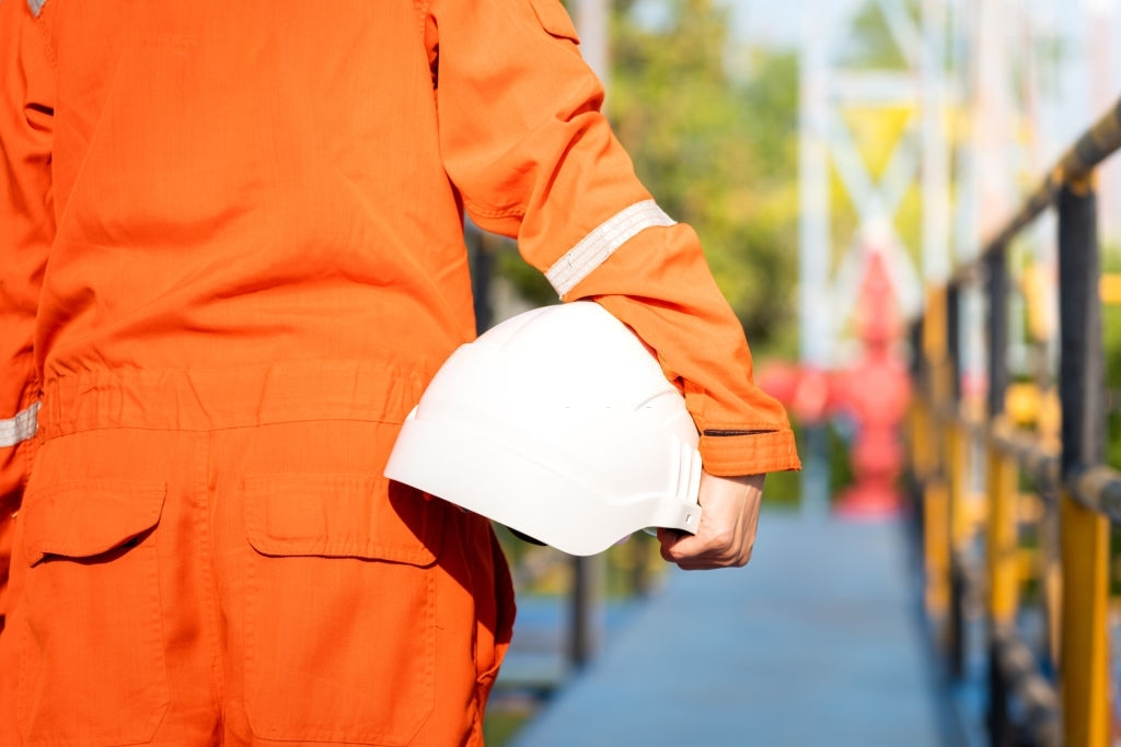 Oil field operator or worker is holding white safety hardhat, prepare to start the job on working platform (as background). Safety in operation concept photo.